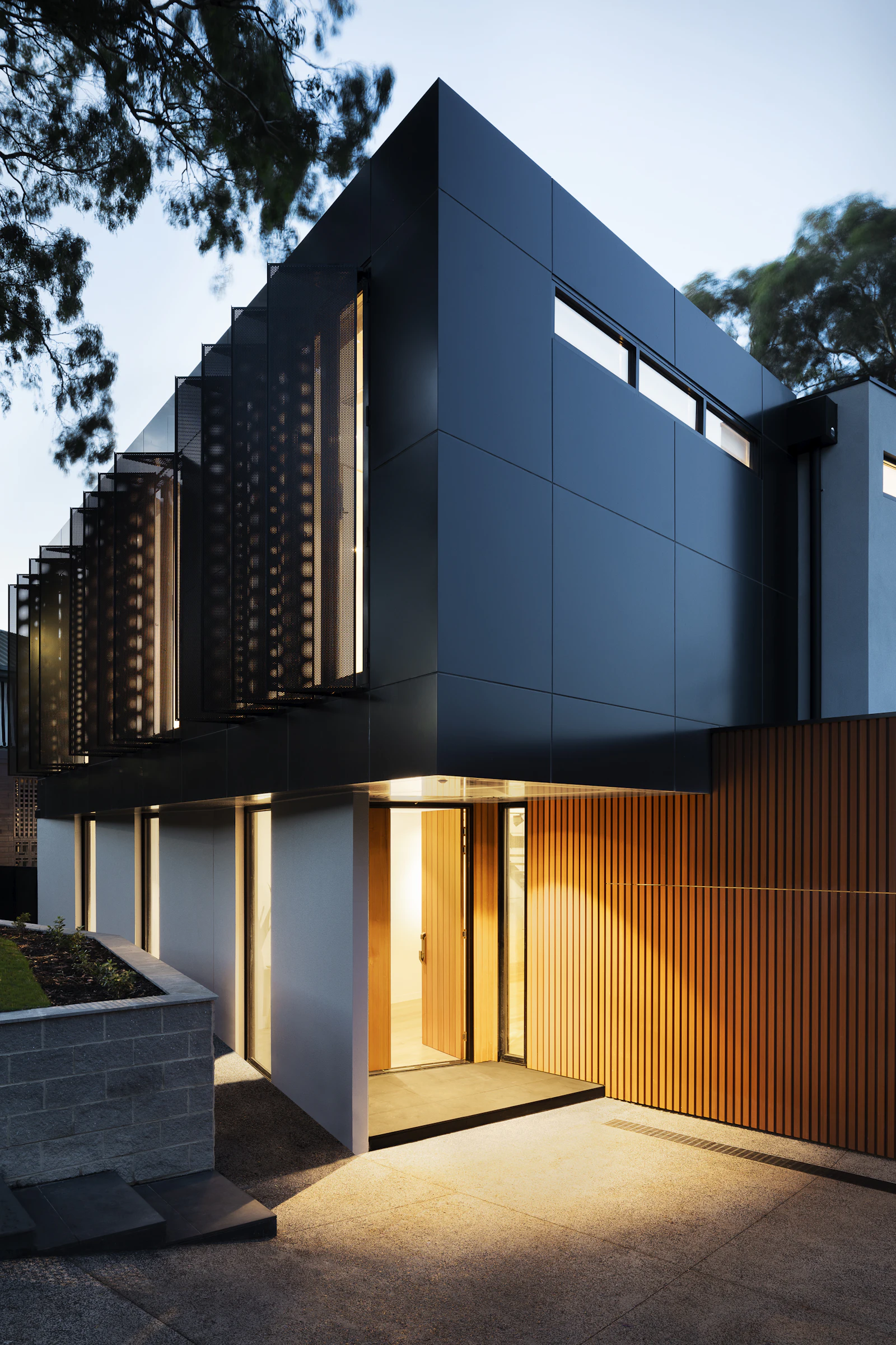 Dark-clad contemporary house with timber louvres at dusk